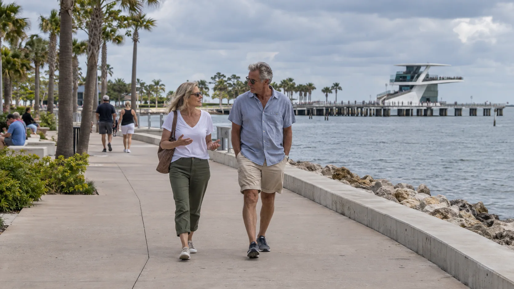 Two fictional adults over 50 walking on a Florida bayfront promenade with St. Pete Pier in the background